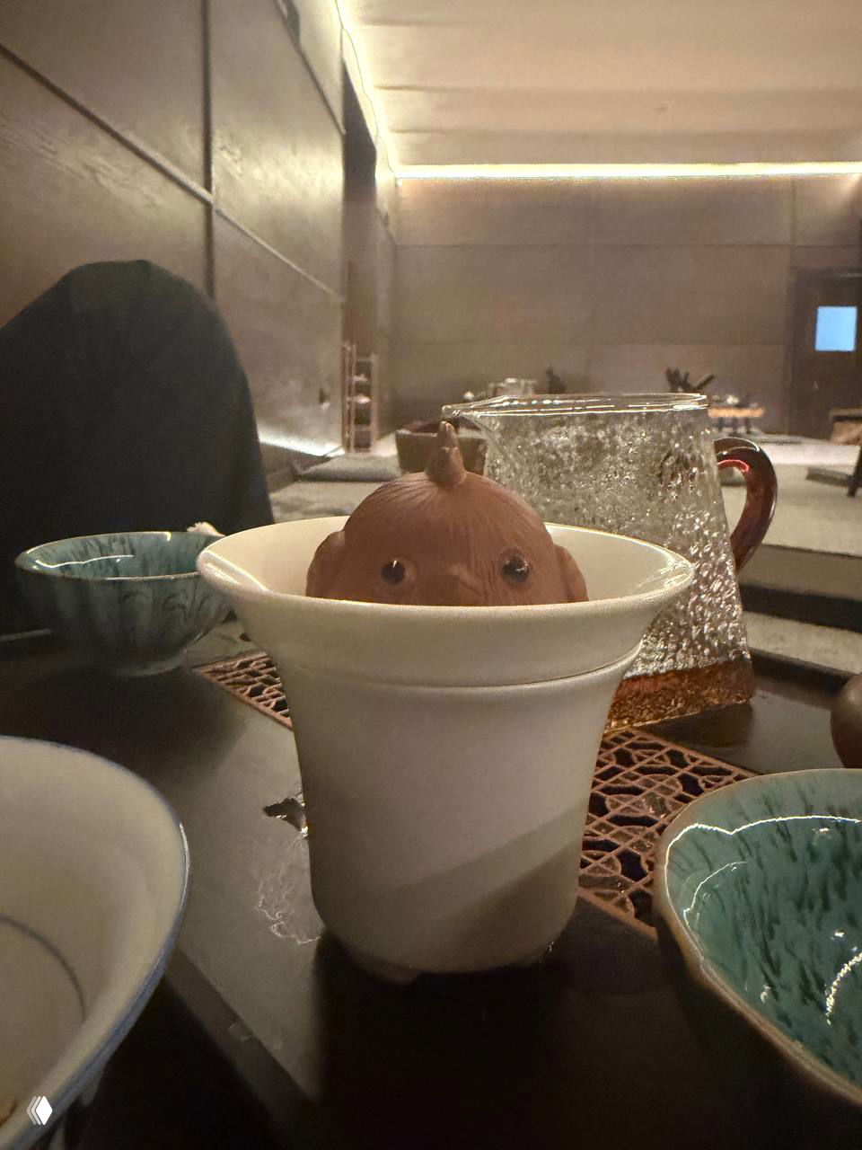 Крупный план на чайный сервиз: гайвань с керамической крышкой в чашке, прозрачный чайник и пиалы на подносе во время чаепития.