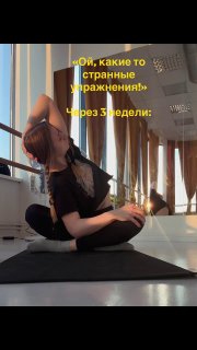 Женщина в спортивной одежде выполняет глубокую растяжку на коврике в светлой фитнес‑студии; в кадре видны зеркала, большие окна и жёлтая надпись на фото.