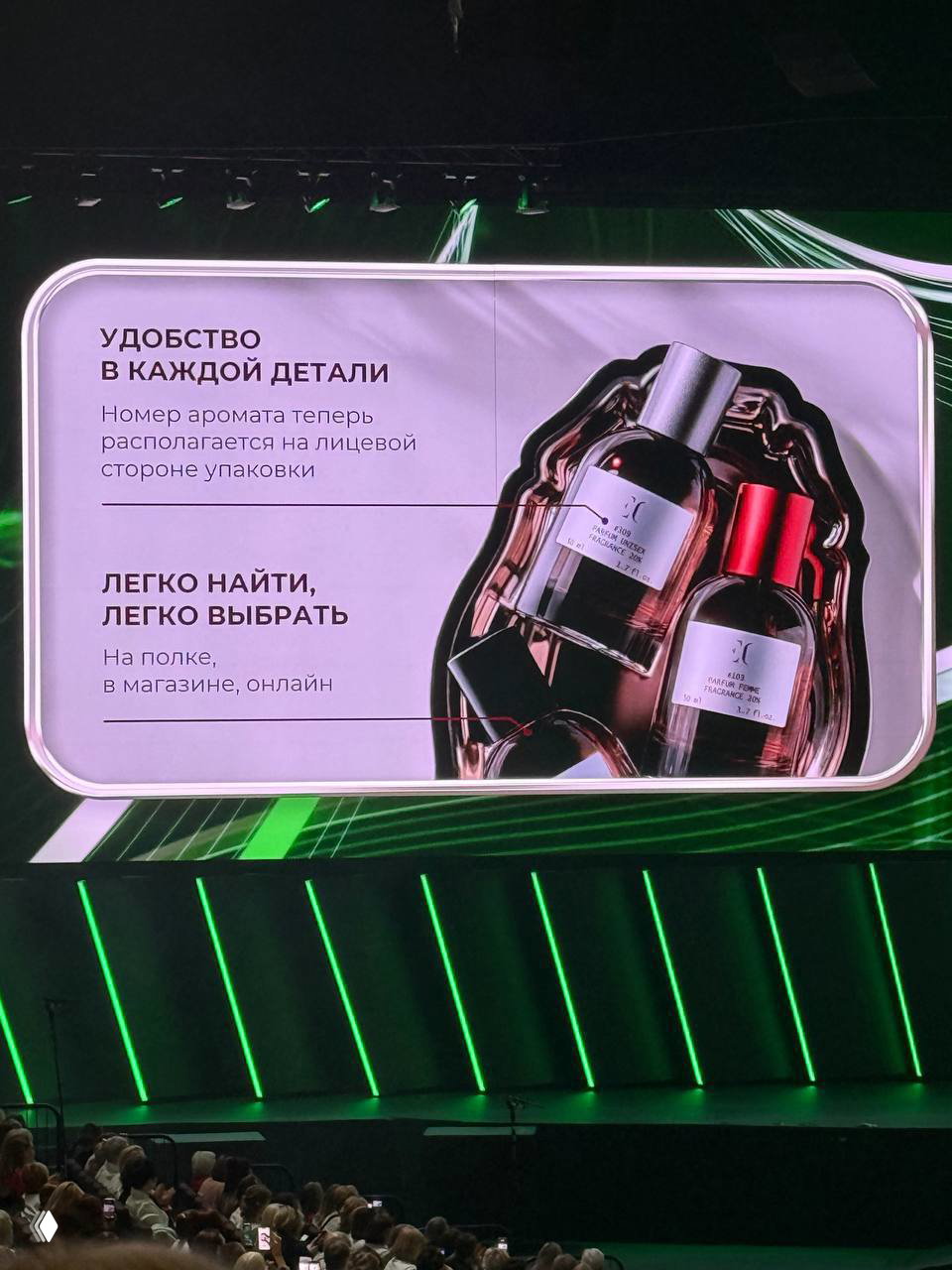 Информационный слайд: флаконы Enjoy Care крупным планом и текст о номере аромата на лицевой стороне упаковки; сцена и зрители частично видны.