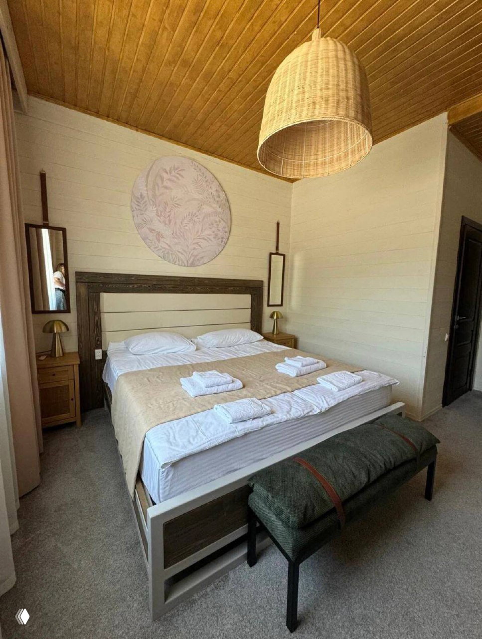 Светлый комфортабельный номер с большой кроватью, тёплыми тонами интерьера, ночными тумбочками и аккуратно разложенными полотенцами.