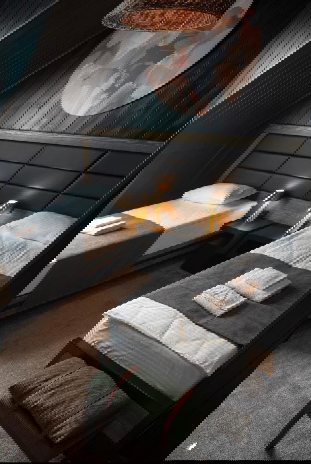 Уютная мансардная комната с тёмной деревянной отделкой, двумя раздельными кроватями и аккуратными полотенцами на постели.