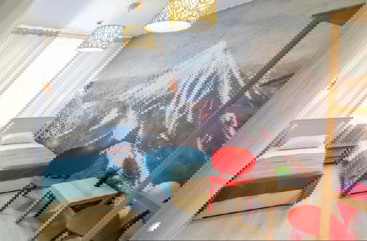 Яркая гостиная с двумя односпальными кроватями на фоне фрески гор, красочные стулья и светлый пол — атмосферный интерьер.