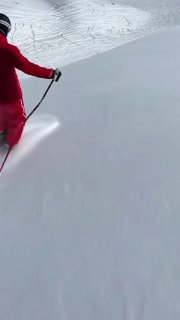 Человек в красной куртке едет фрирайдом по гладкому белому склону Авачинского перевала; виден пыльный след и снежный склон.