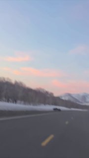 Размытое фото с дороги на Камчатке: тёмный силуэт на дороге (возможно медведь), на горизонте горы и розовые облака.