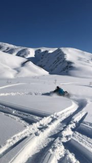 Снегоход в действии на фоне заснеженных гор Камчатки: человек на технике, глубокий пушистый снег, видны следы и ясное голубое небо.