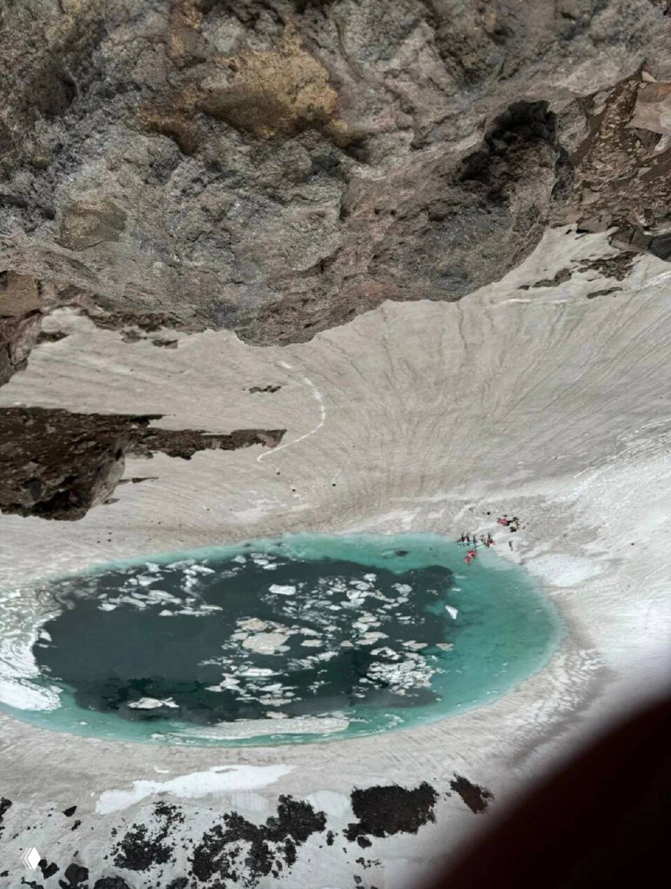Вид внутрь кратера Горелого: бирюзовое озеро с ледяными плавучими льдинами и группа туристов у береговой линии на снегу.