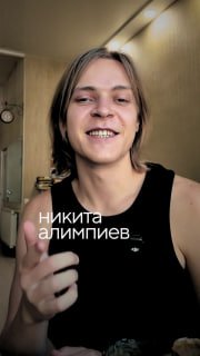 Улыбающийся молодой мужчина крупным планом в интерьере, снят в селфи‑стиле; на кадре видно наложенный белый текст и мягкое освещение, атмосфера офиса.